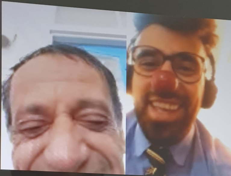 An older man in an elderly home in Palestine is encountered joyfully by a male clown and smiles.