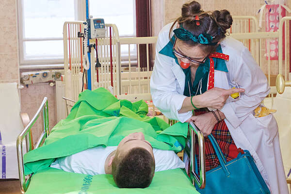 A boy is on his way to surgery and a female clown from PIROS ORR is cheering him up as she stands next to him