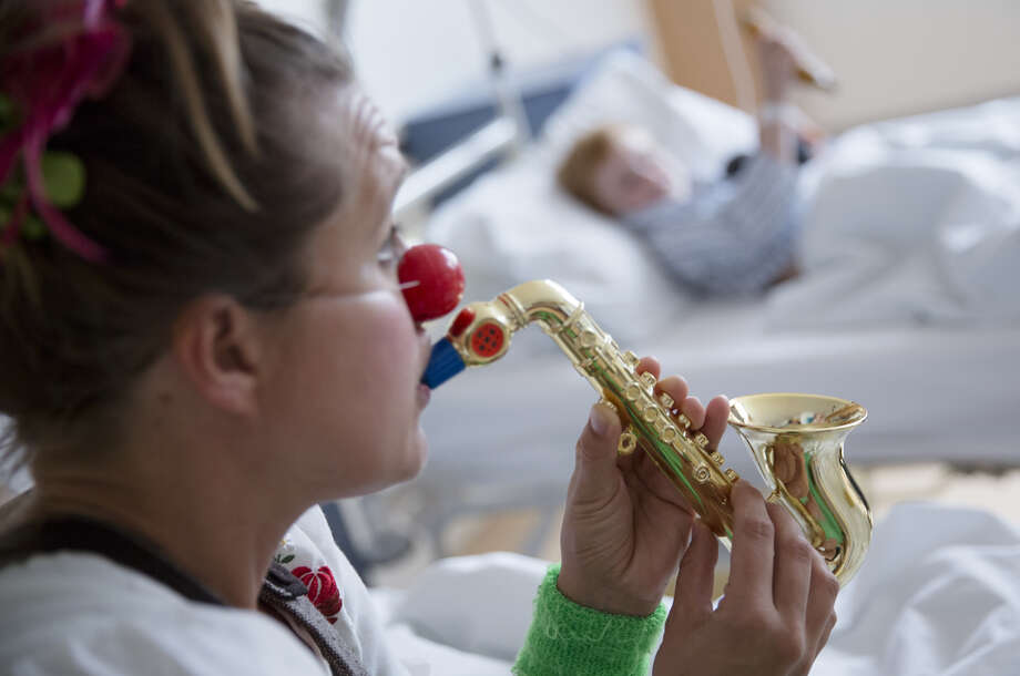 Female clown playing the saxophone to boy in hospital room