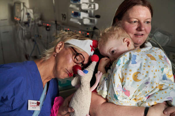A female clown stands next to a little boy and his mother, encouraging them before the heart surgery