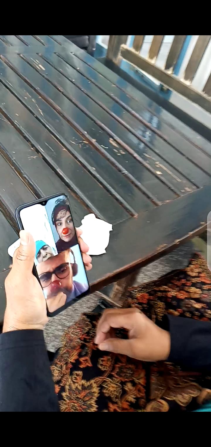 An older woman in Palestine watches two clowns on the screen of a mobile phone and smiles.
