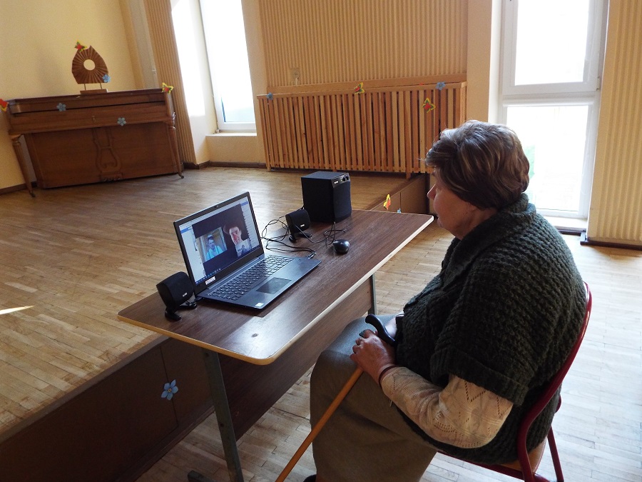 An old woman watches a clown intervention online as she sits in front of a laptop in a big empty hall in her elderly care home in Lithuania