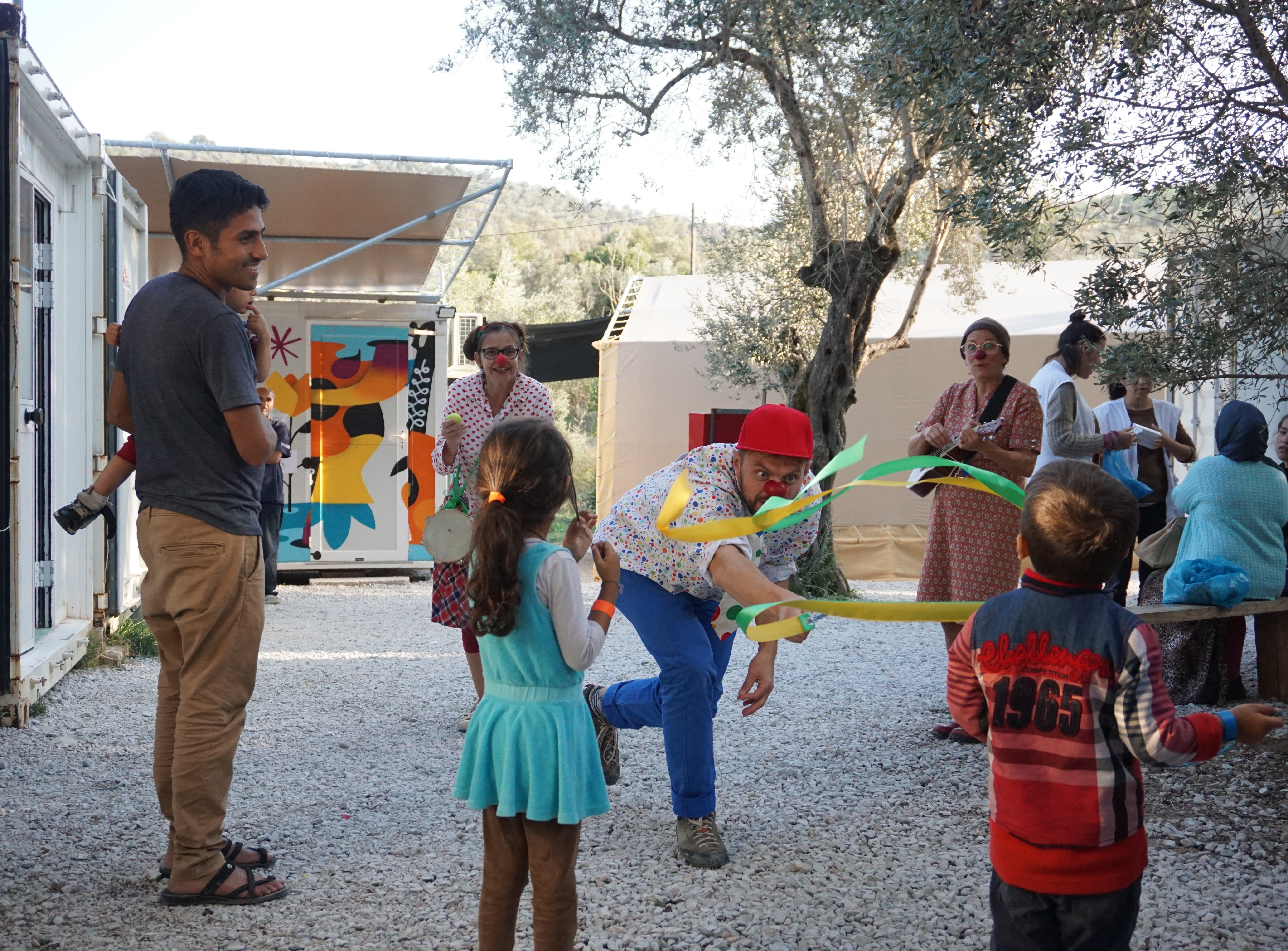 RED NOSES clowns interact with children in the MORIA refugee camp by performing tricks to make them smile